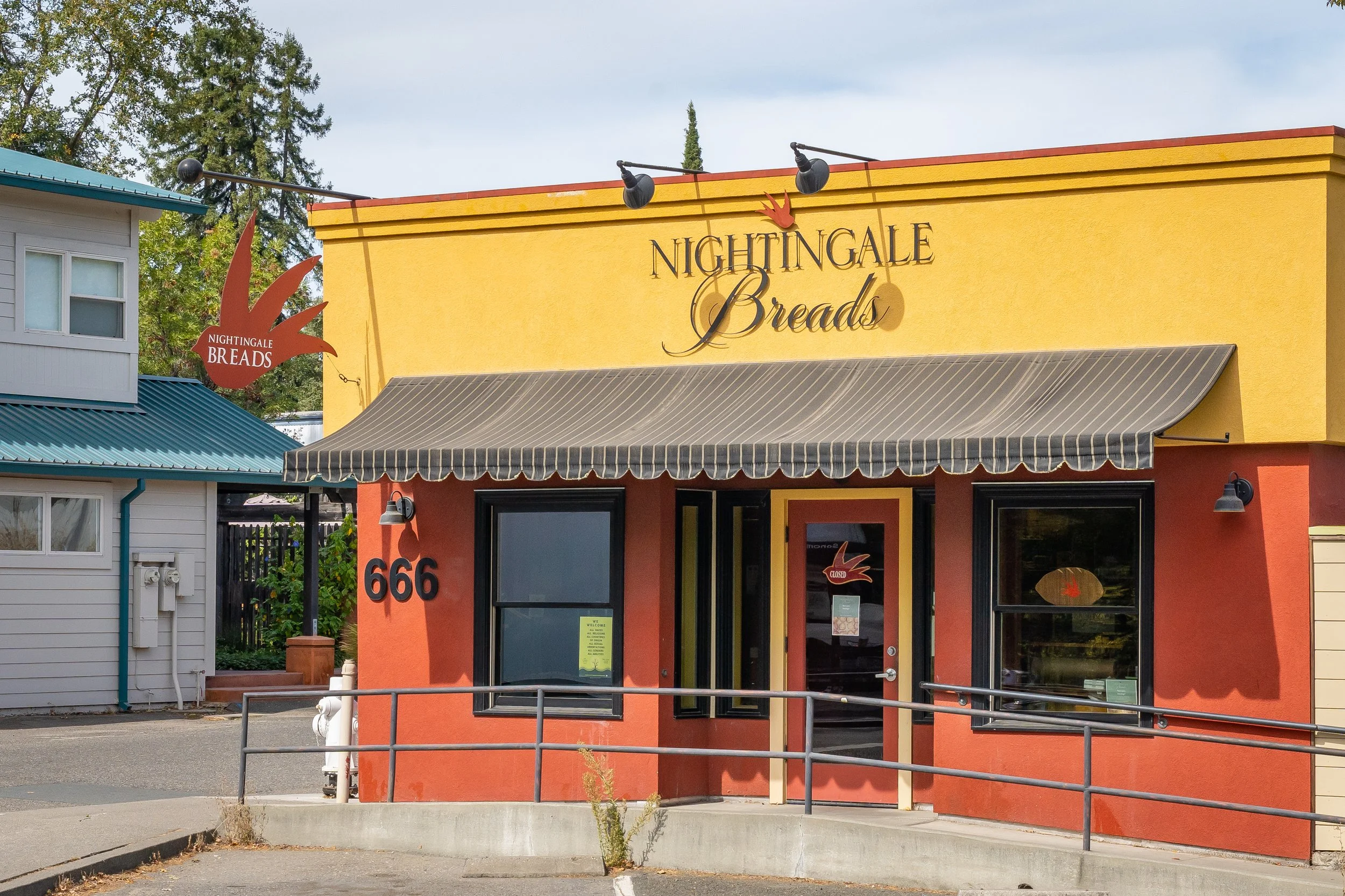 Front of a bakery named Nightingale Breads with a yellow facade, striped awning, and green 