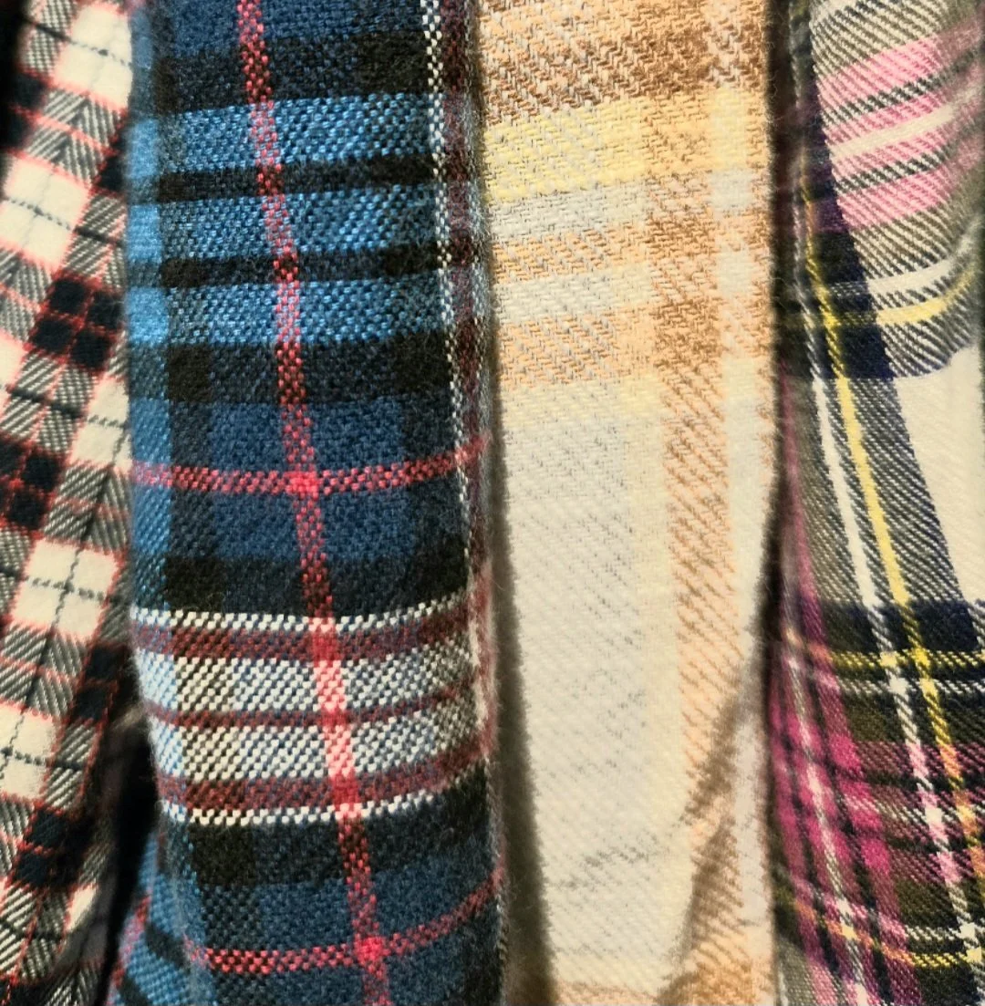 Another, different close-up of overlapping, folded flannel shirts with different color patterns and textures