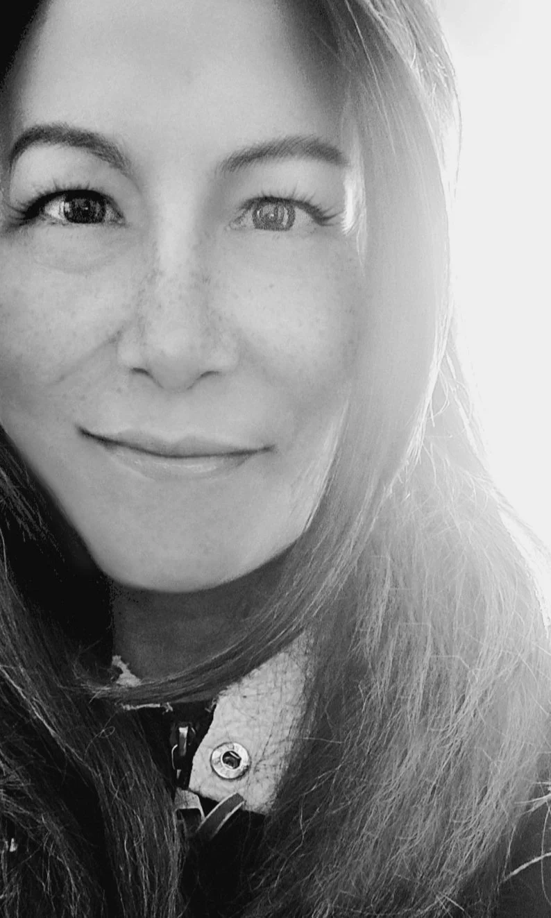 Close-up black-and-white photo of a woman with long hair, smiling slightly, with a soft background.