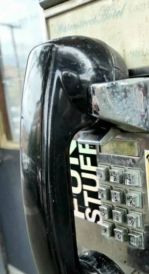 Close-up of an old, black payphone with a chrome keypad showing wear and grime.