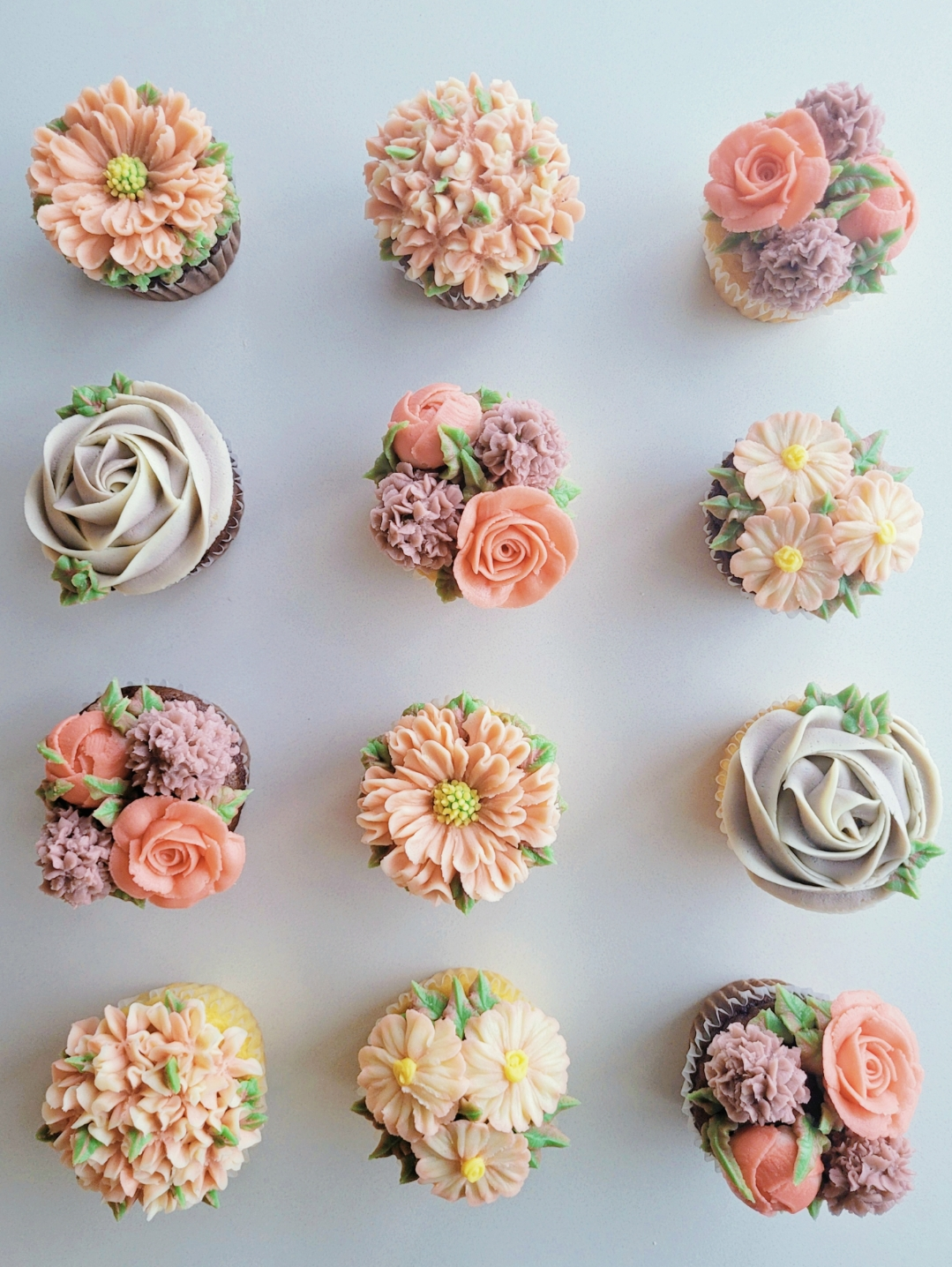 Assorted decorative cupcakes with floral frosting designs arranged in rows on a white background.