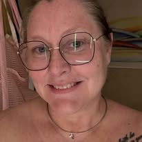 A woman with glasses smiling in a close-up photo, with books and shelves in the background.