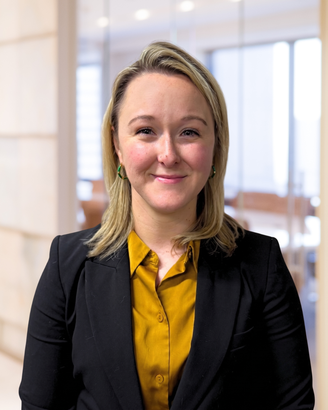 A woman in a business suit smiling in an office setting.