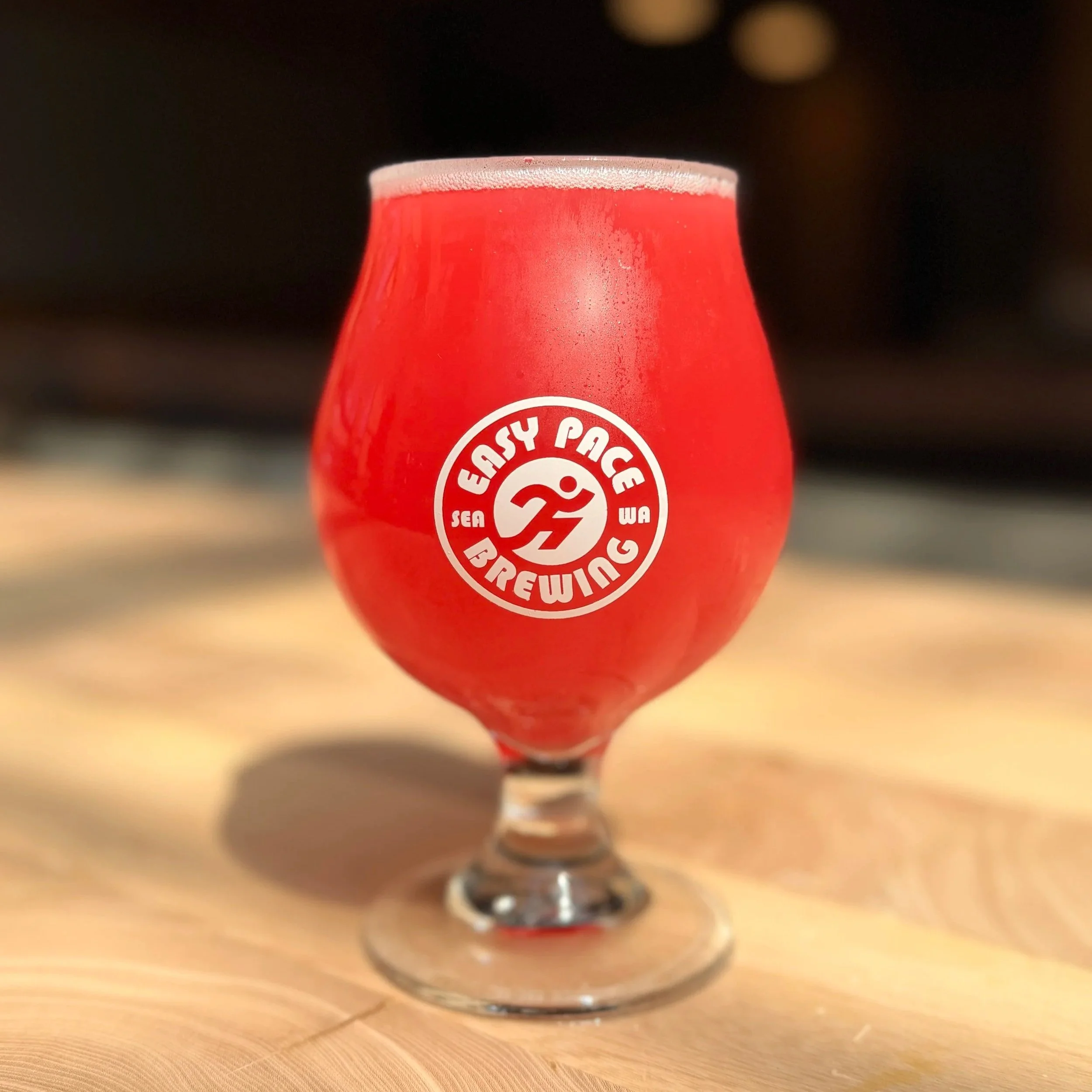 Close-up of a glass of red beer with a foamy head, sitting on a wooden surface.