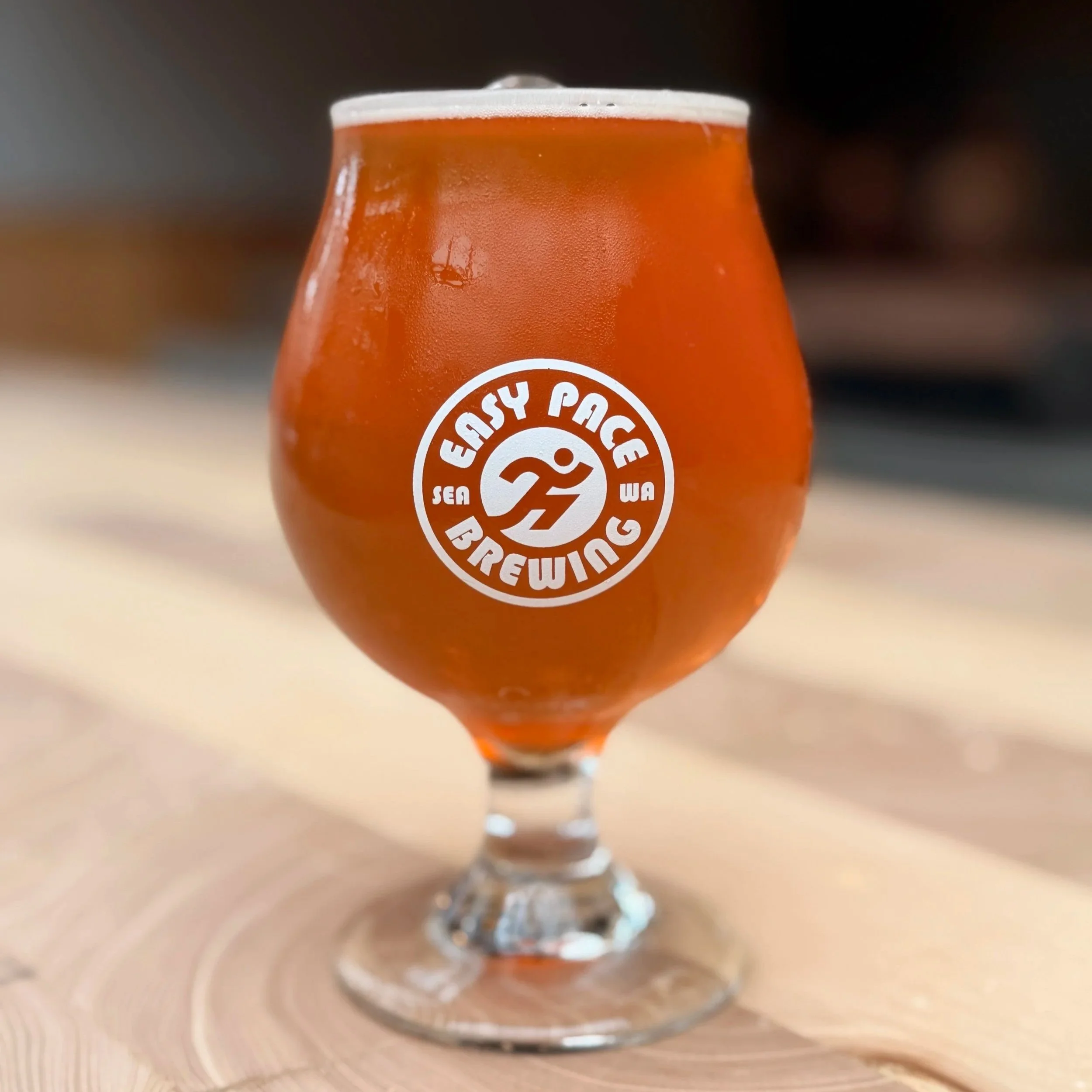 Close-up of a glass of amber-colored beer with a frothy head, placed on a wooden surface.