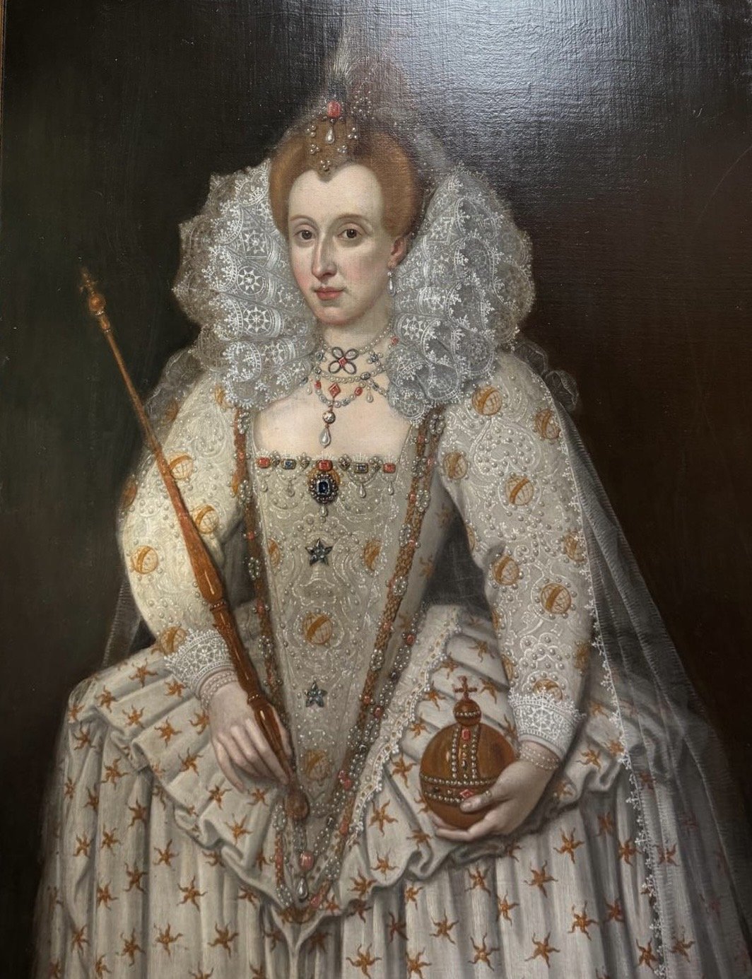 Queen Anne of England and Scotland, dressed in elaborate royal attire, holding a scepter in one hand and a crown in the other, wearing a large lace collar and ornate jewelry.