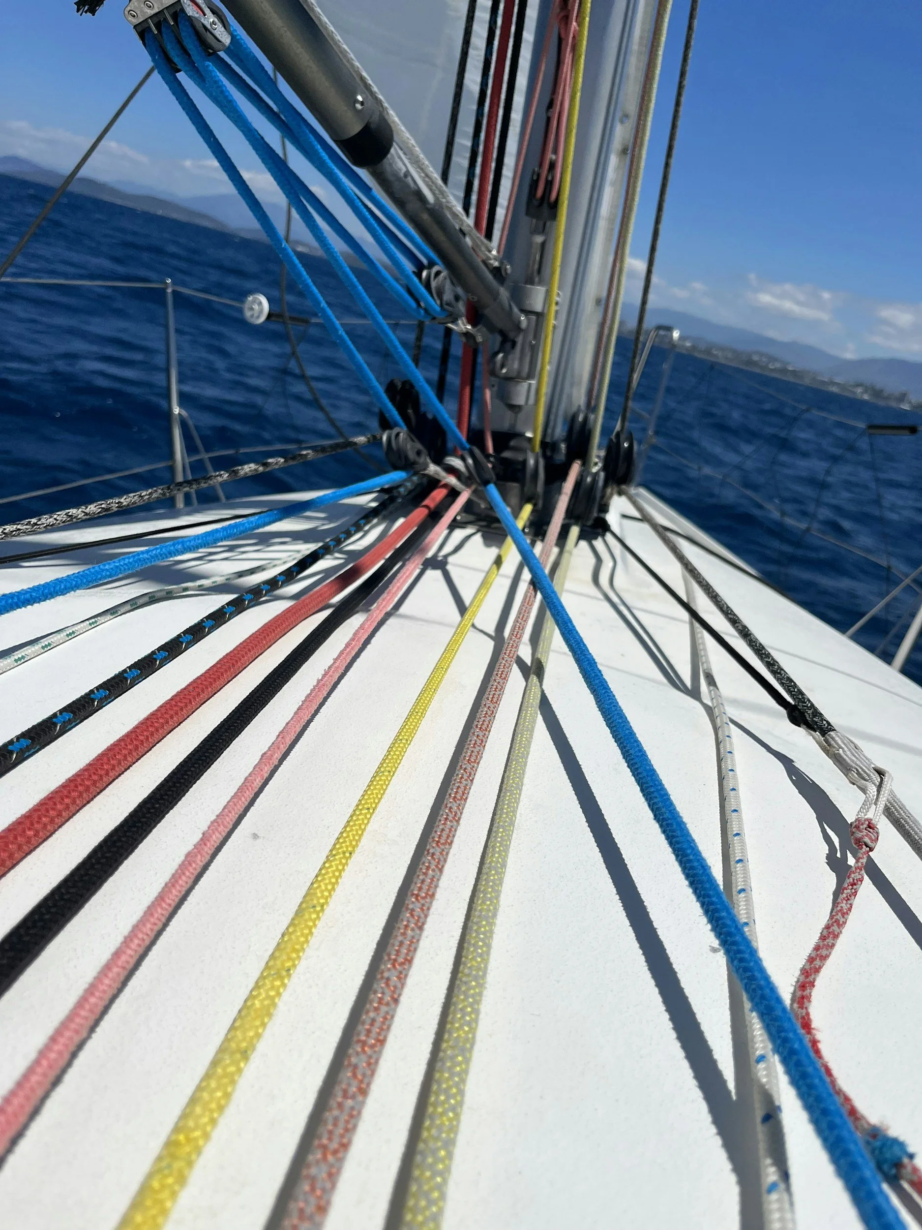 Close-up view of the rigging lines and pulleys on a sailboat, with the ocean and sky in the background.