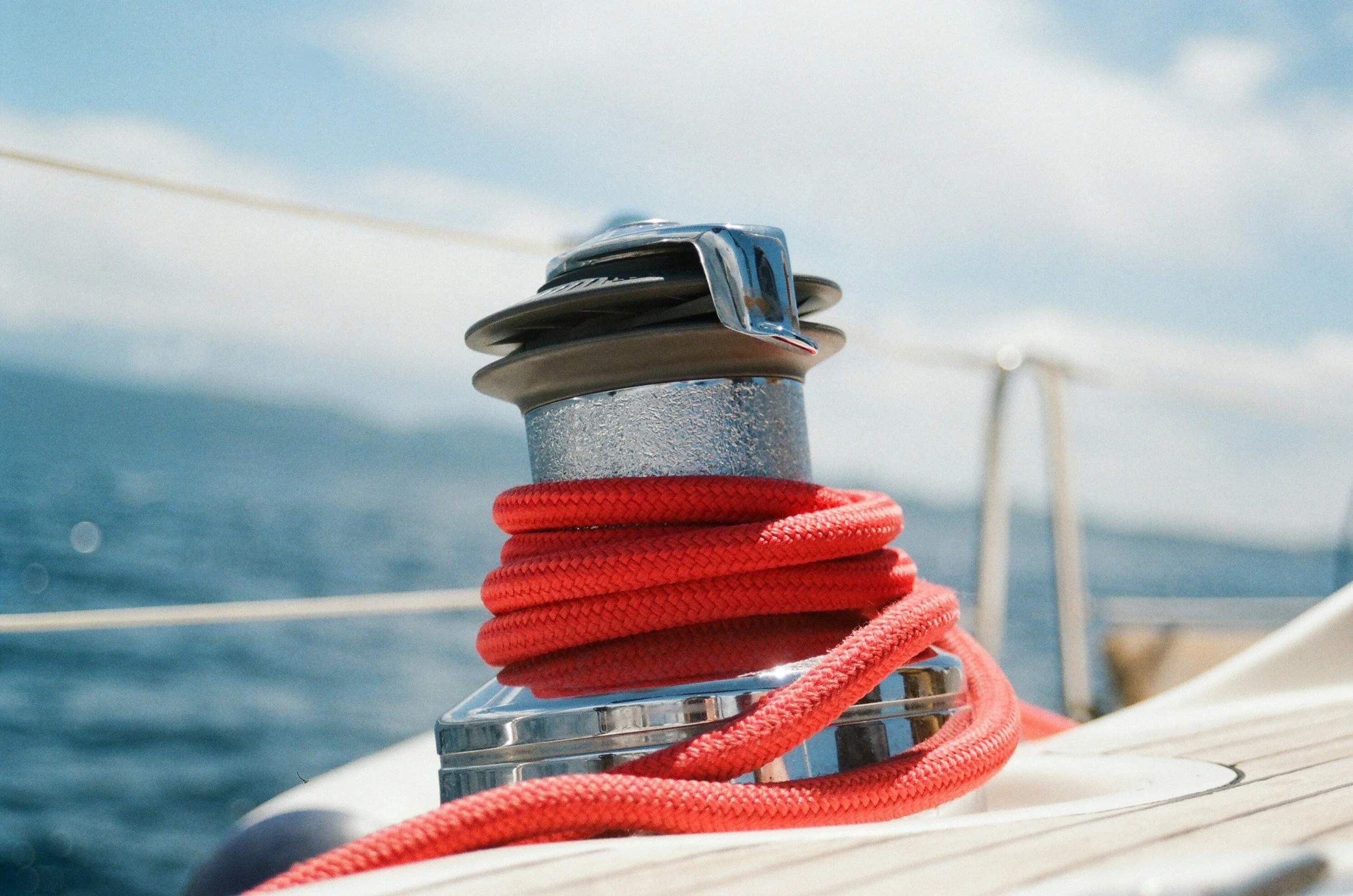 Close-up of a red rope wrapped around a metal cleat on a boat, with the ocean in the background and a distant bridge.