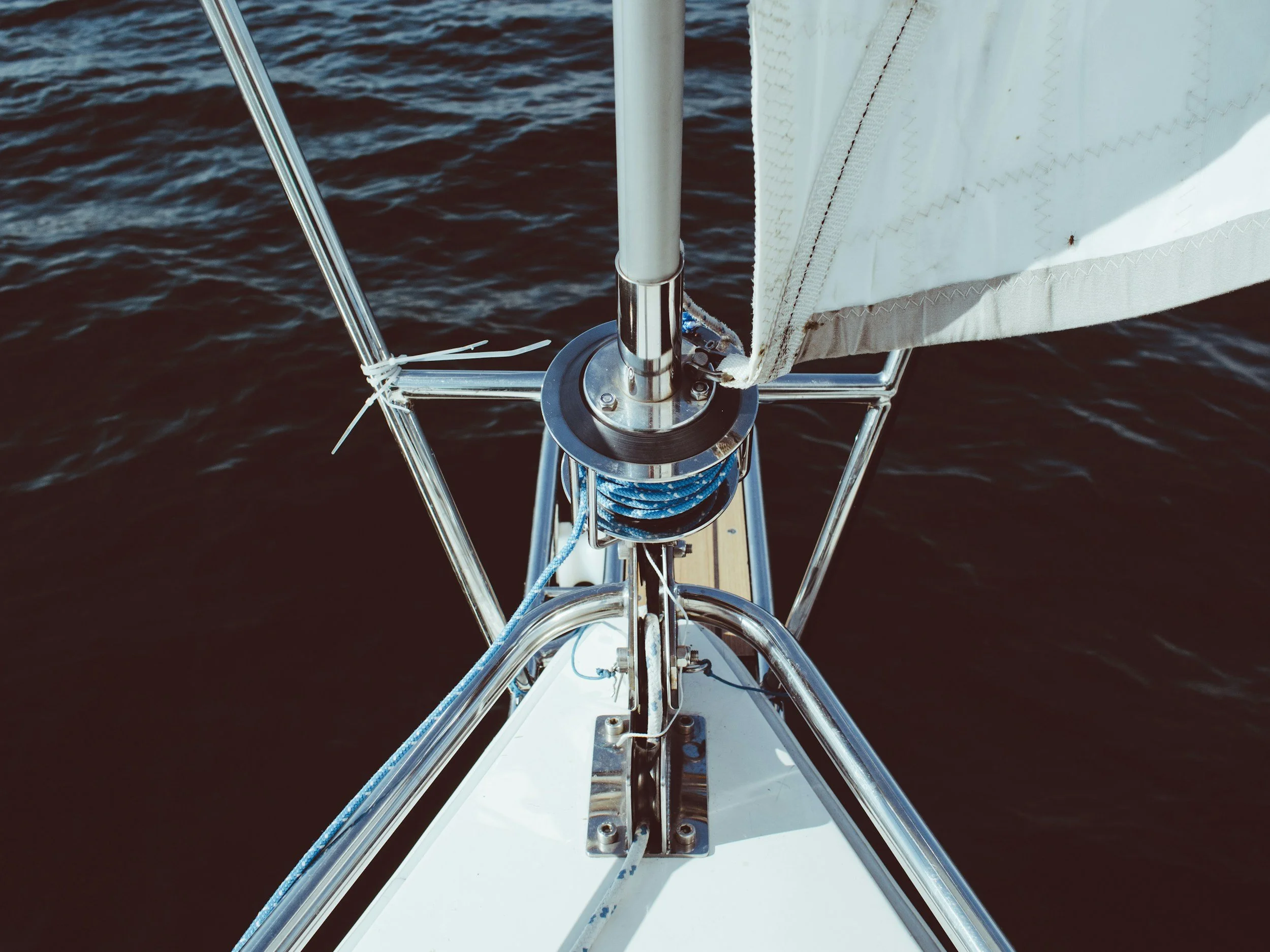 View from the bow of a sailboat showing the mast, rigging, and a portion of the sail against dark water.