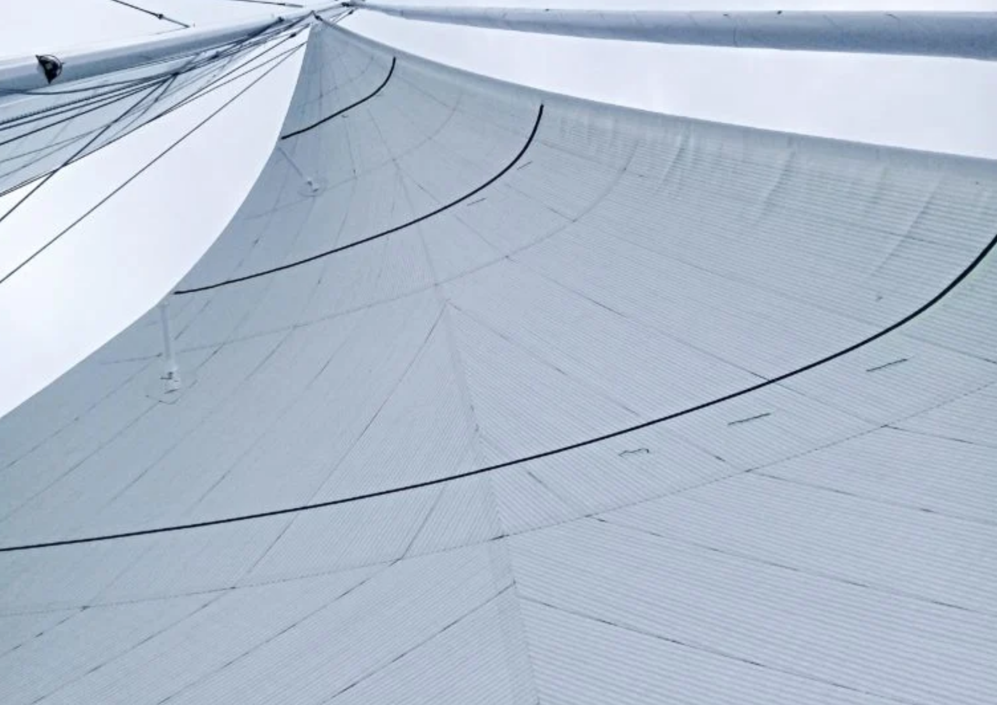 Close-up of a white sailboat sail with black lines and rigging, captured from below against a cloudy sky.