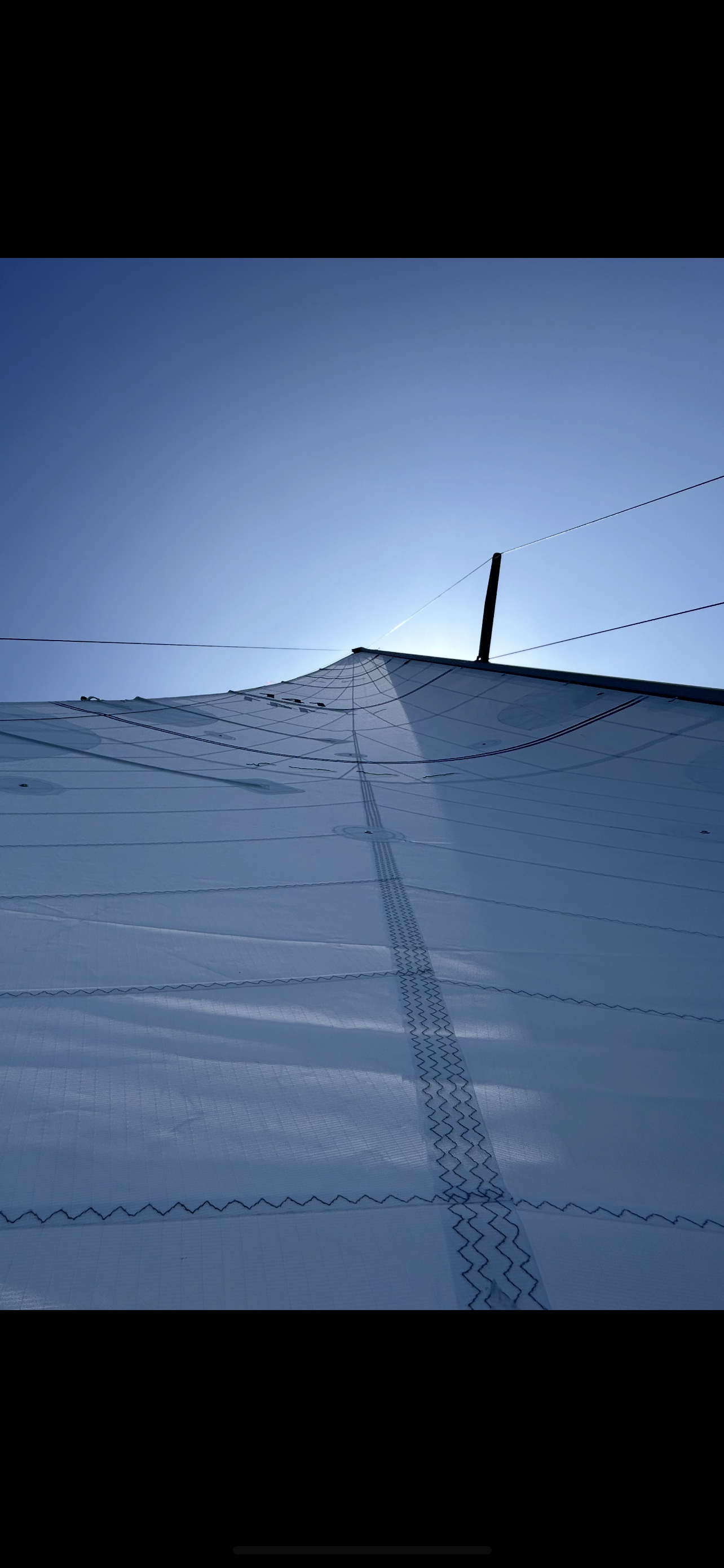 Close-up of a white sailboat sail with black lines and rigging, captured from below against a cloudy sky.