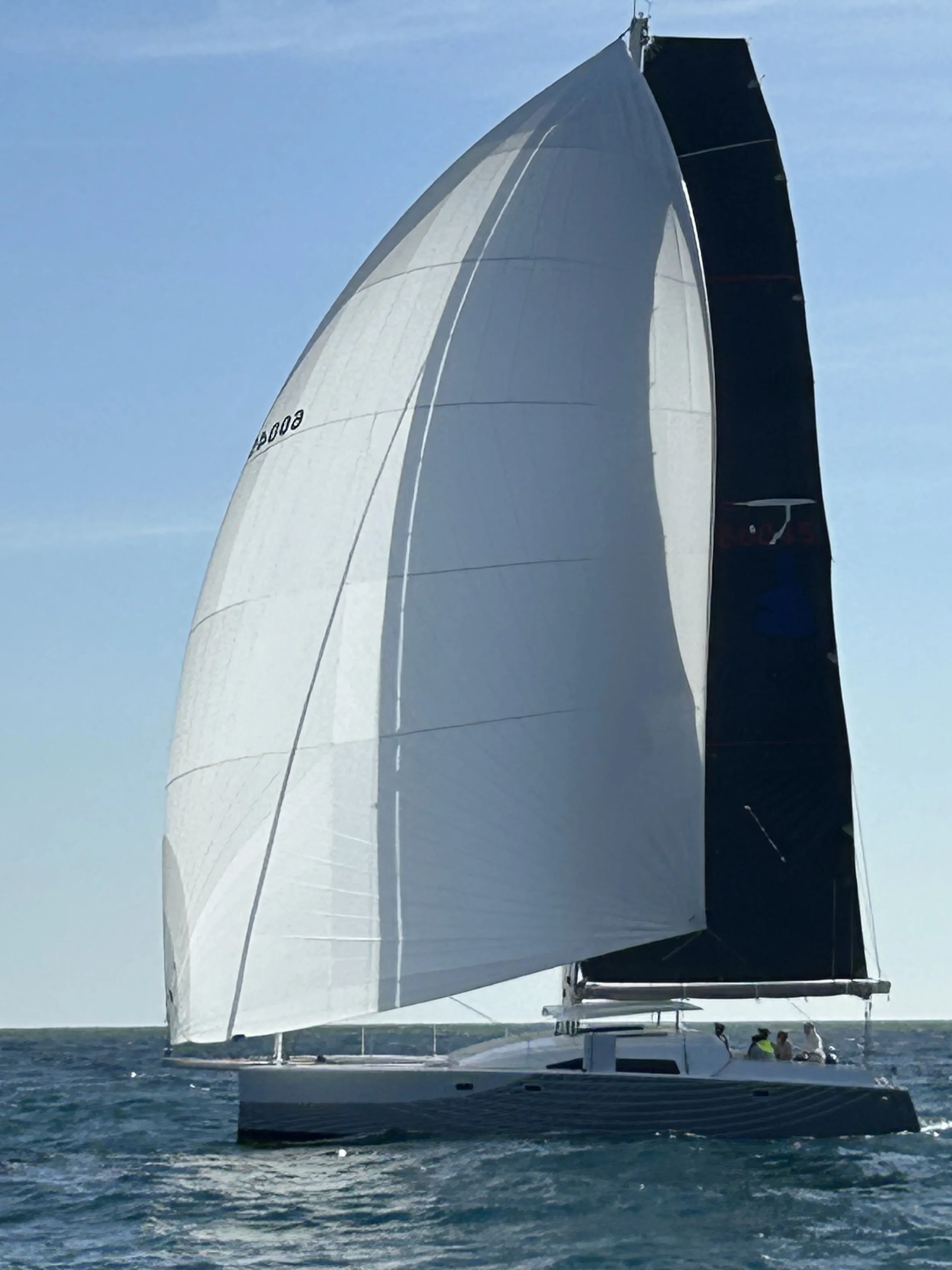 A sailboat with large white sails on the water with a clear blue sky in the background.