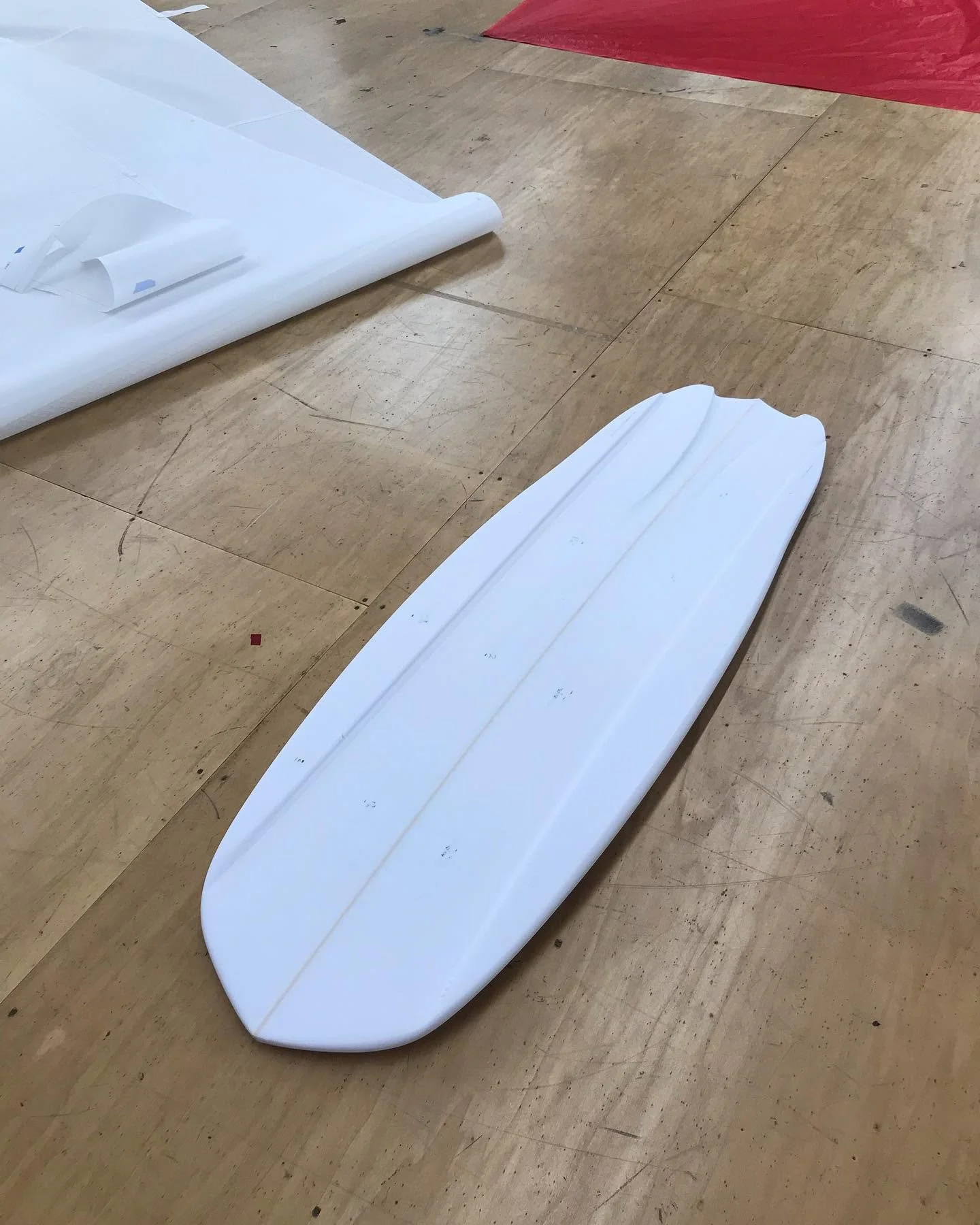 A large white racing sled on a wooden floor with a red mat partially visible in the background.