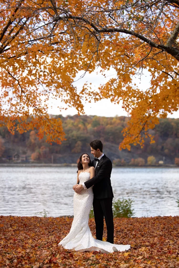 Bride and Groom by a Lake Surrounded by Fall Foliage at a Wedding Planned by Faith Ferguson Productions