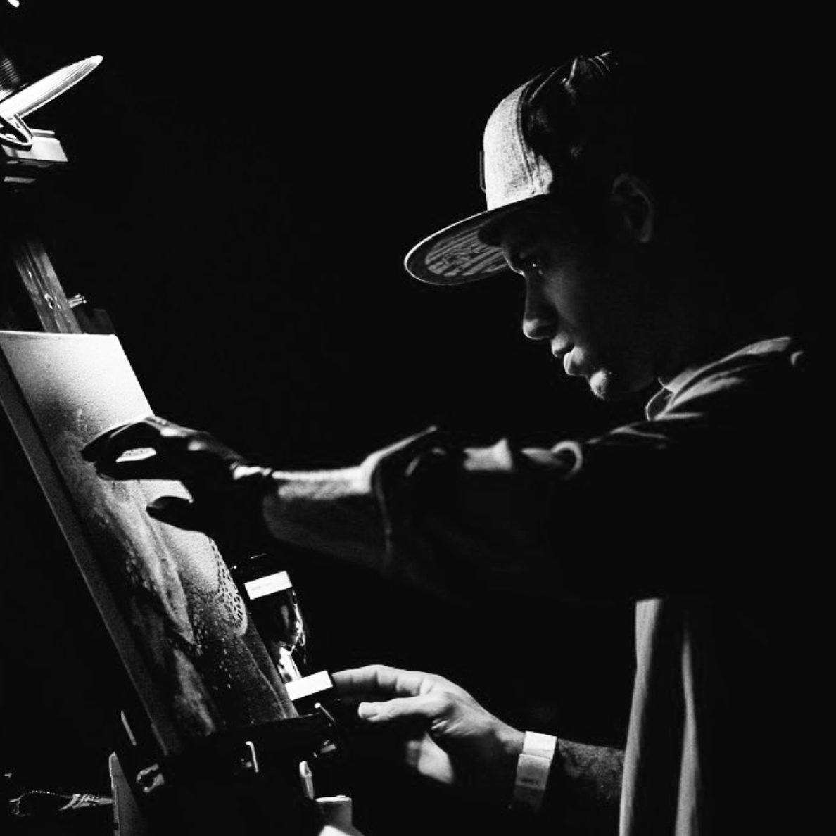 A person wearing a baseball cap and gloves is working on an arcade game or slot machine in a dark setting.