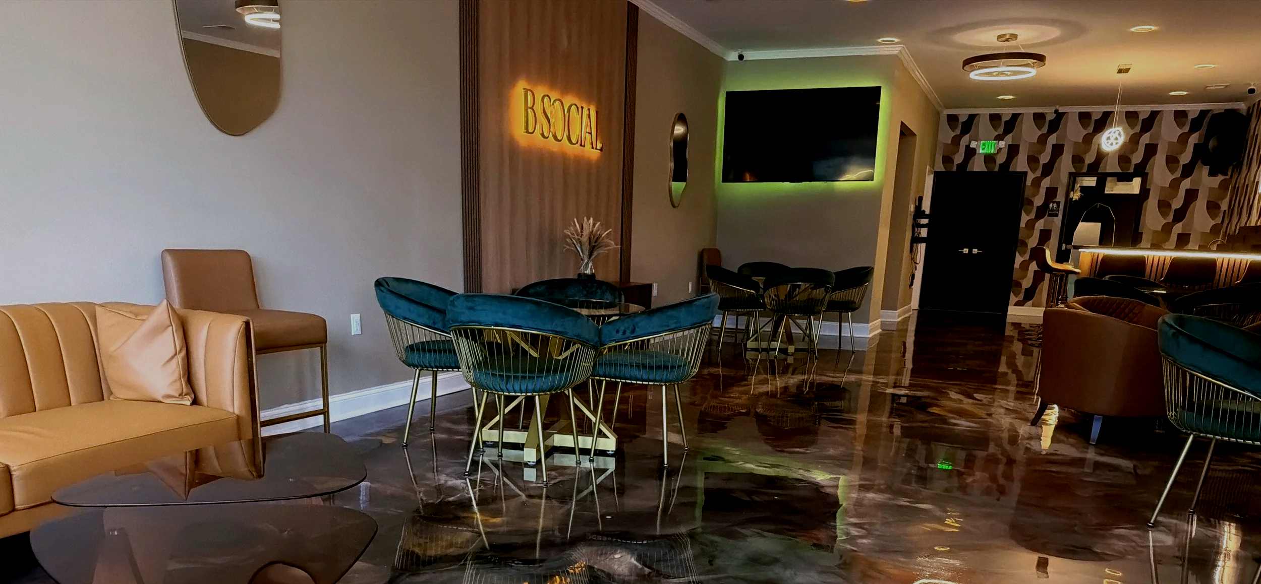 Modern hotel lobby with velvet chairs, a leather bench, wall-mounted TV with green backlight, decorative walls, and exposed ceiling lights.