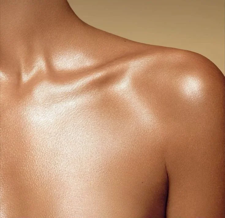 Close-up of a person's shoulder and upper chest with smooth, shiny skin and a golden beige background.