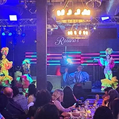 Performers in colorful costumes dancing on stage at Rosaritos, with an audience seated at tables watching.