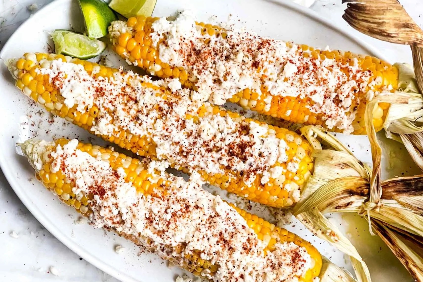 Grilled corn on the cob topped with crumbled cheese, red chili powder, and served with lime wedges.