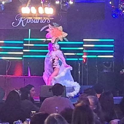 Performer in costume on stage at Rosaro's, with audience seated in front.