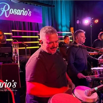 Band performing on stage at Rosario's, with musicians playing various instruments and colorful stage lighting.