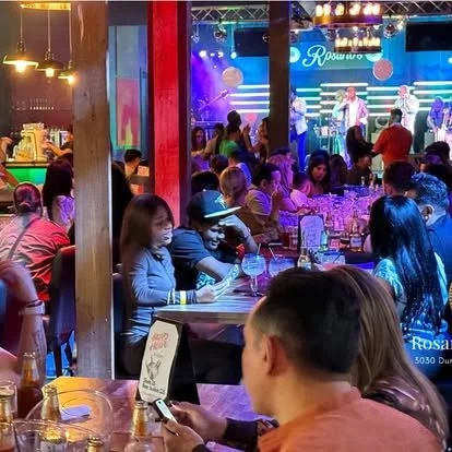 People dining at tables in a lively, colorful concert venue with a stage and musicians performing in the background.