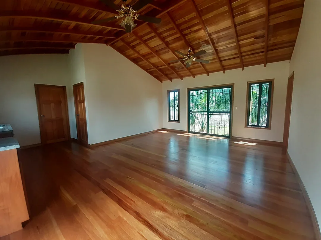 Empty room with wooden floors, a wooden ceiling with two ceiling fans, large windows, and a sliding glass door leading outside.