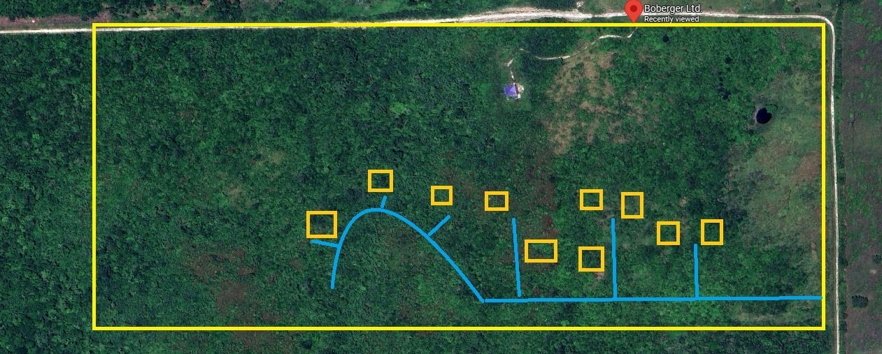 Aerial view of a large green forested area with a yellow boundary outline. Inside, there are multiple blue lines indicating a trail or course, with several yellow square markers along and around the trail. There is a small purple tent near the top center of the enclosed area and a small black circular feature nearby. A road and a label with red text are visible at the top right corner outside the boundary.