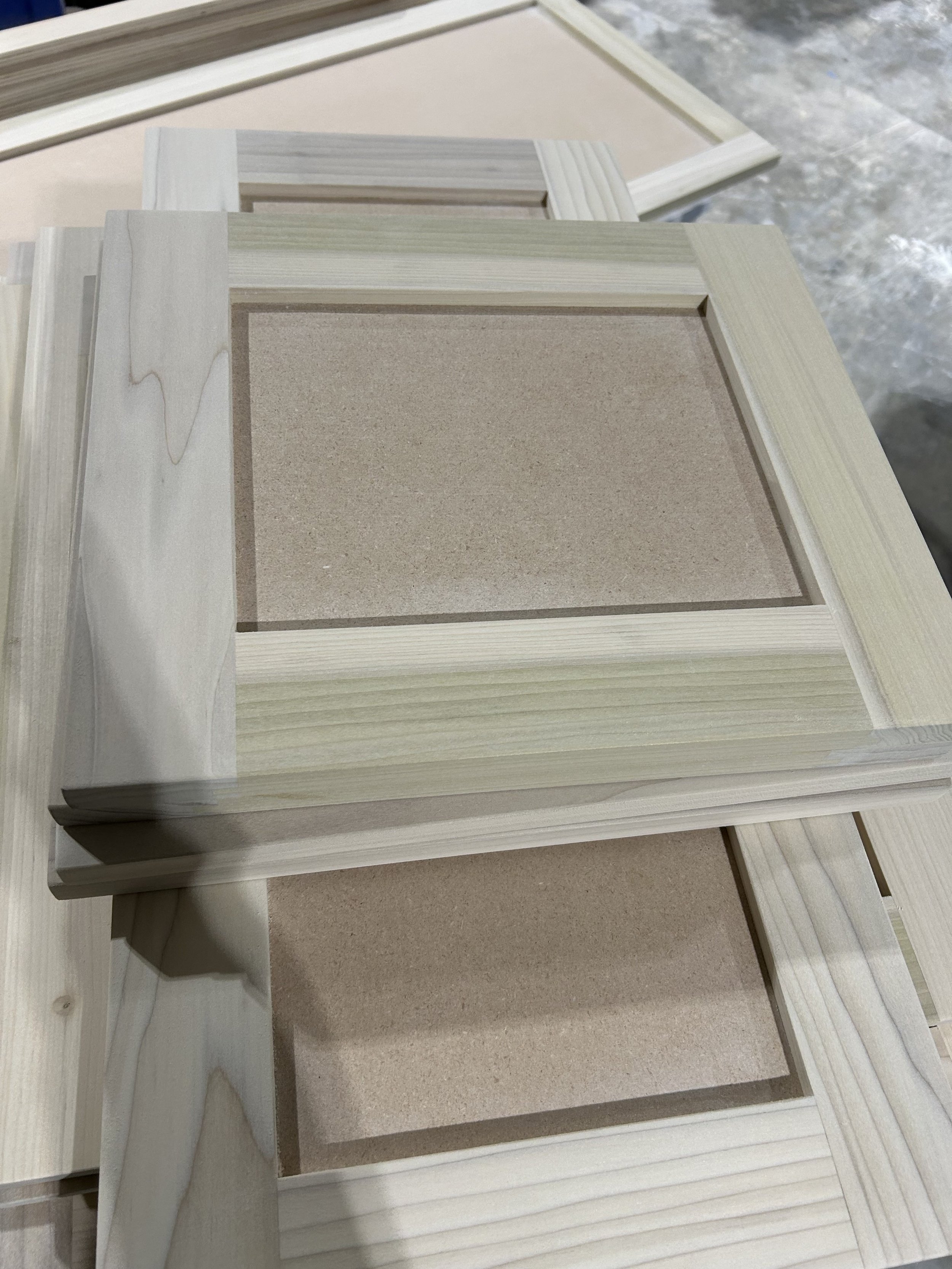Stacked wooden picture frames with glass on a workbench, in a workshop setting.