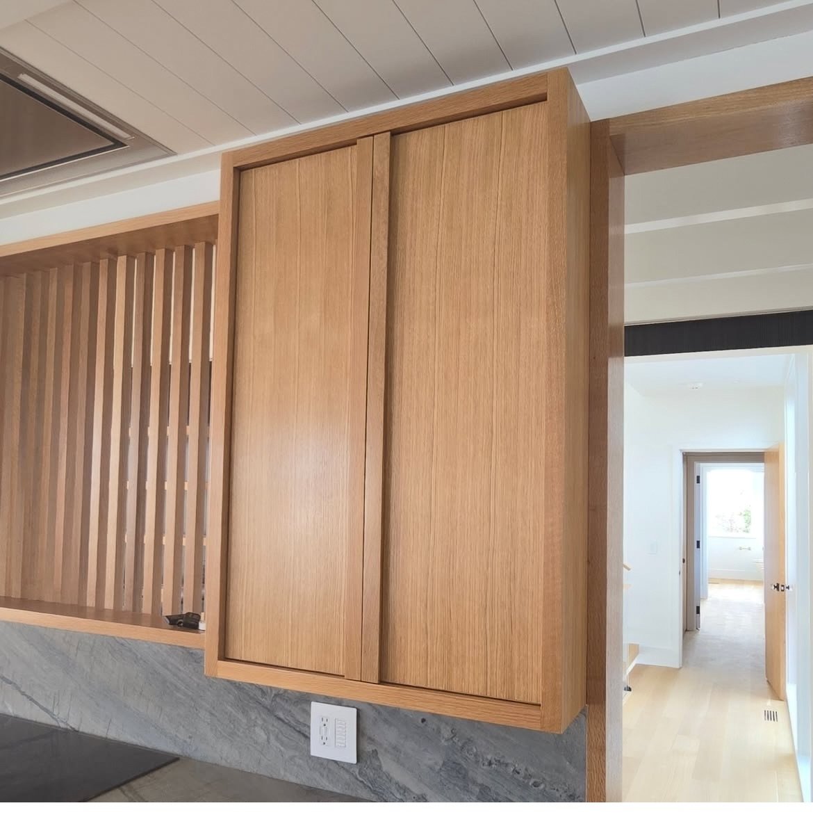 Wooden cabinet with sliding doors in a modern kitchen, featuring a textured marble countertop and a white electrical outlet beneath.