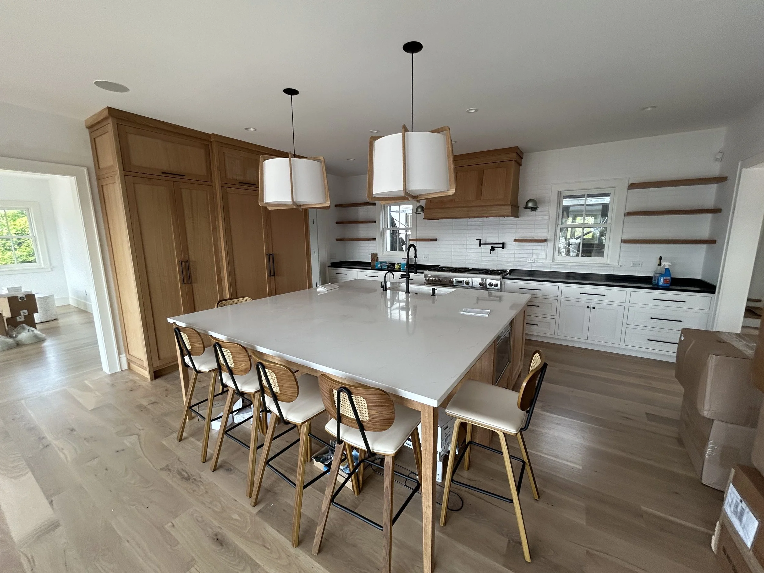 Kitchen with white island, wooden cabinets, white tile backsplash, black faucet, hanging pendant lights, and window