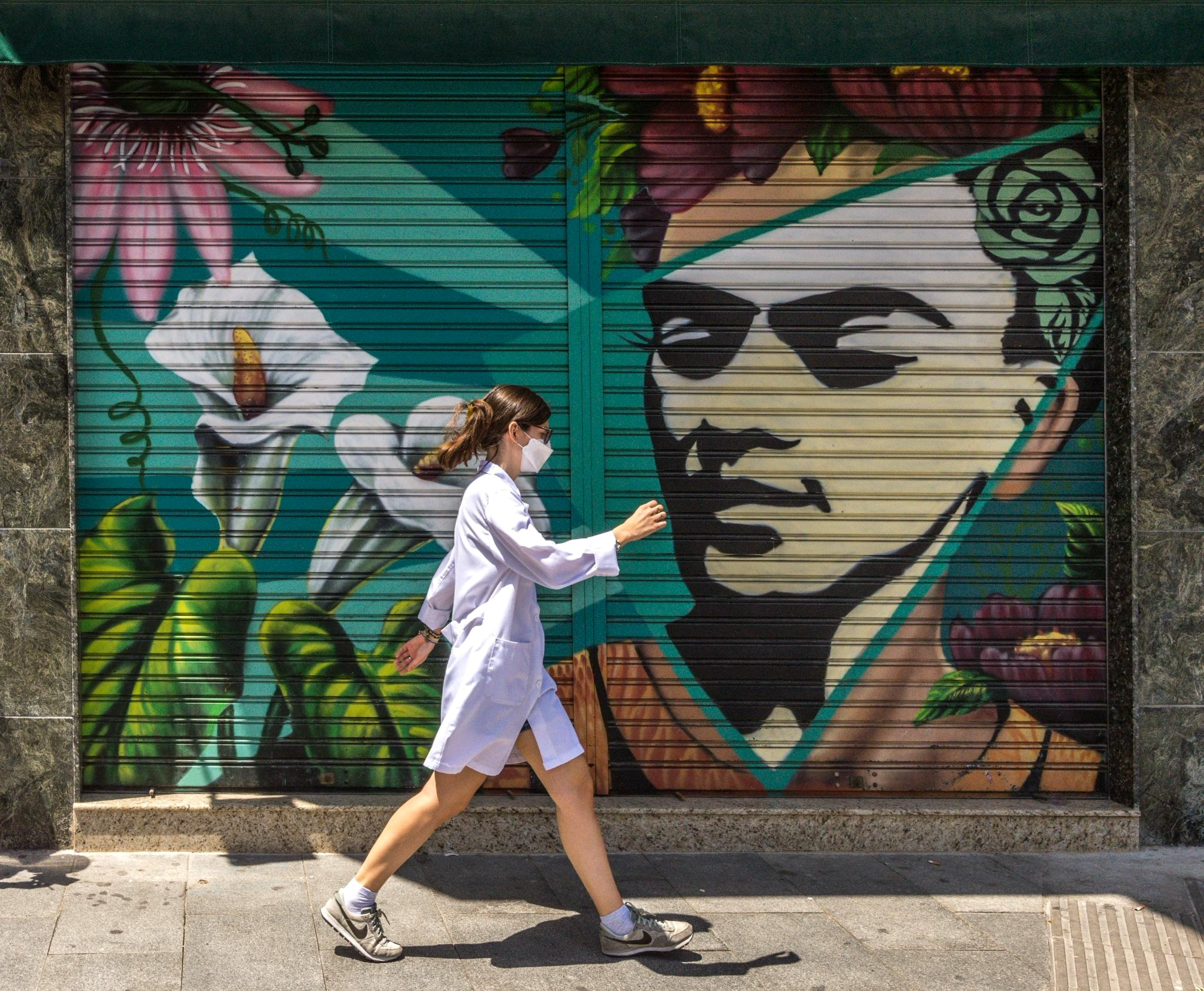 Nurse walking past a street mural in a white coat and mask