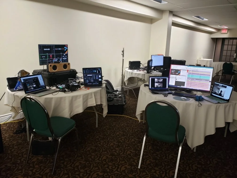 Photo of a banquet room in a hotel with many computers, monitors, speakers and equipment around. No people are in the photo. This image represents the 2021 IIMS, which was held remotely during the COVID-19 pandemic.