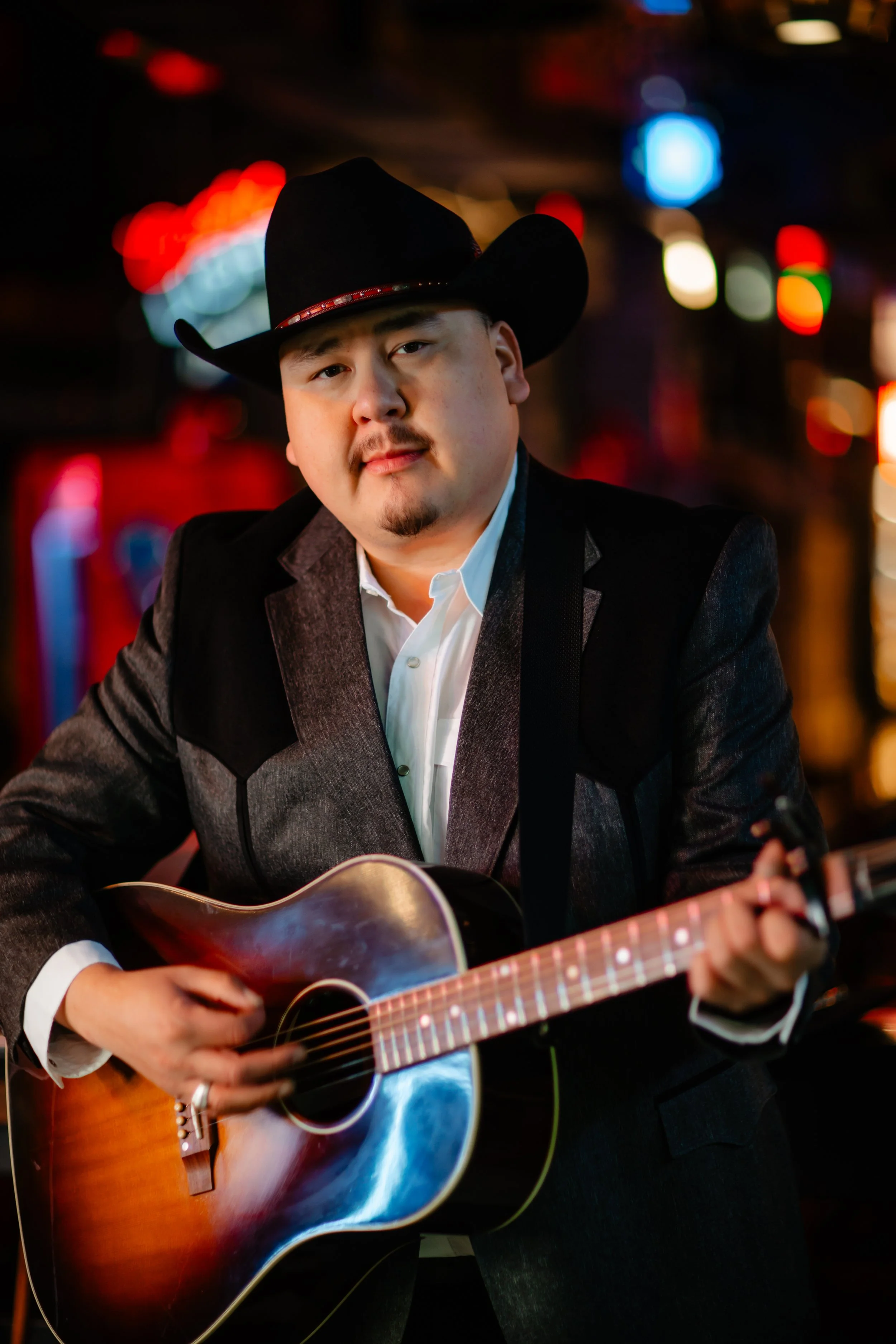A press photo of William Prince strumming a guitar with neon bar lights in the background.