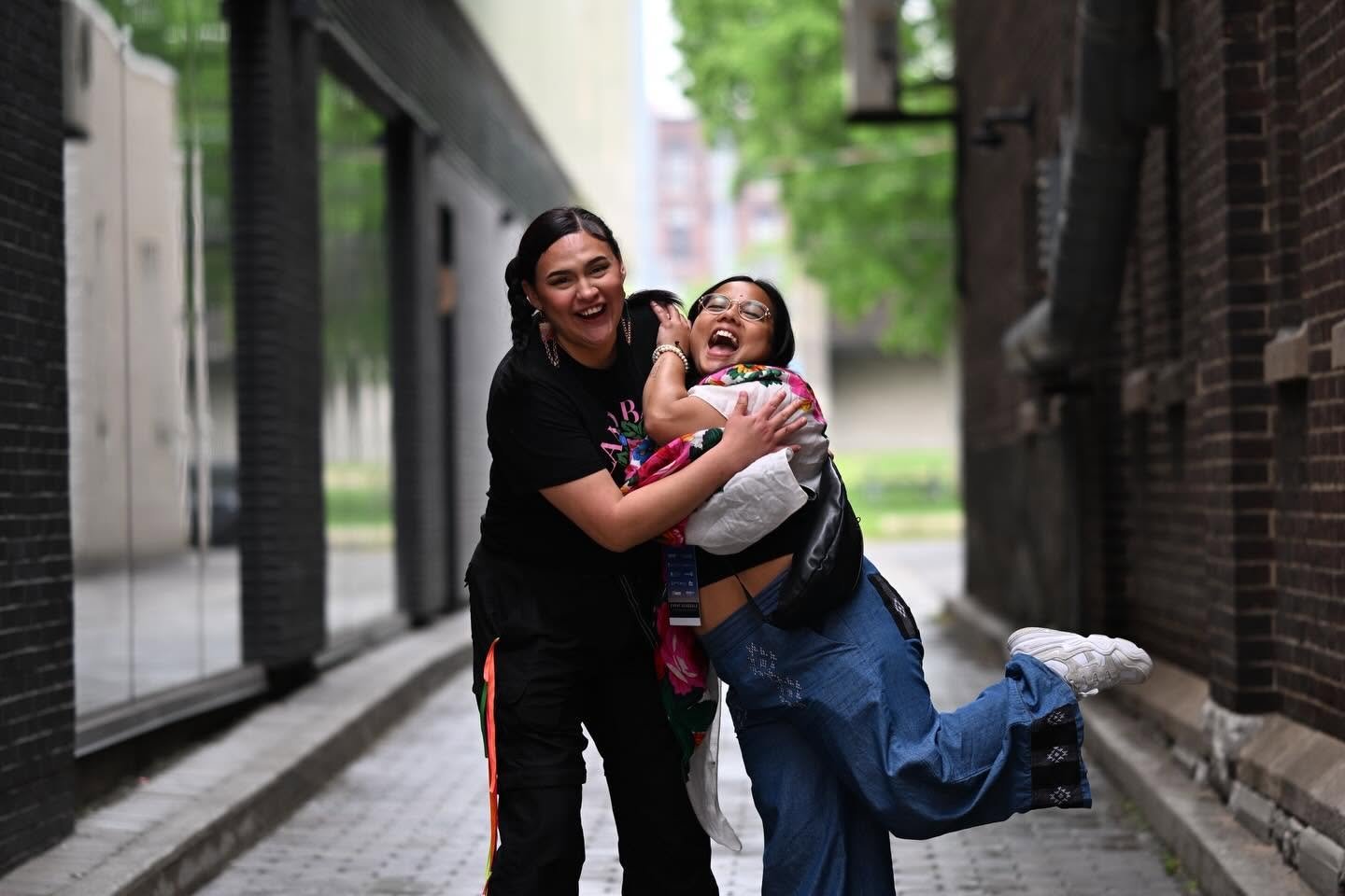 Two female attendees are looking at the camera while smiling, hugging and hamming it up for the camera..