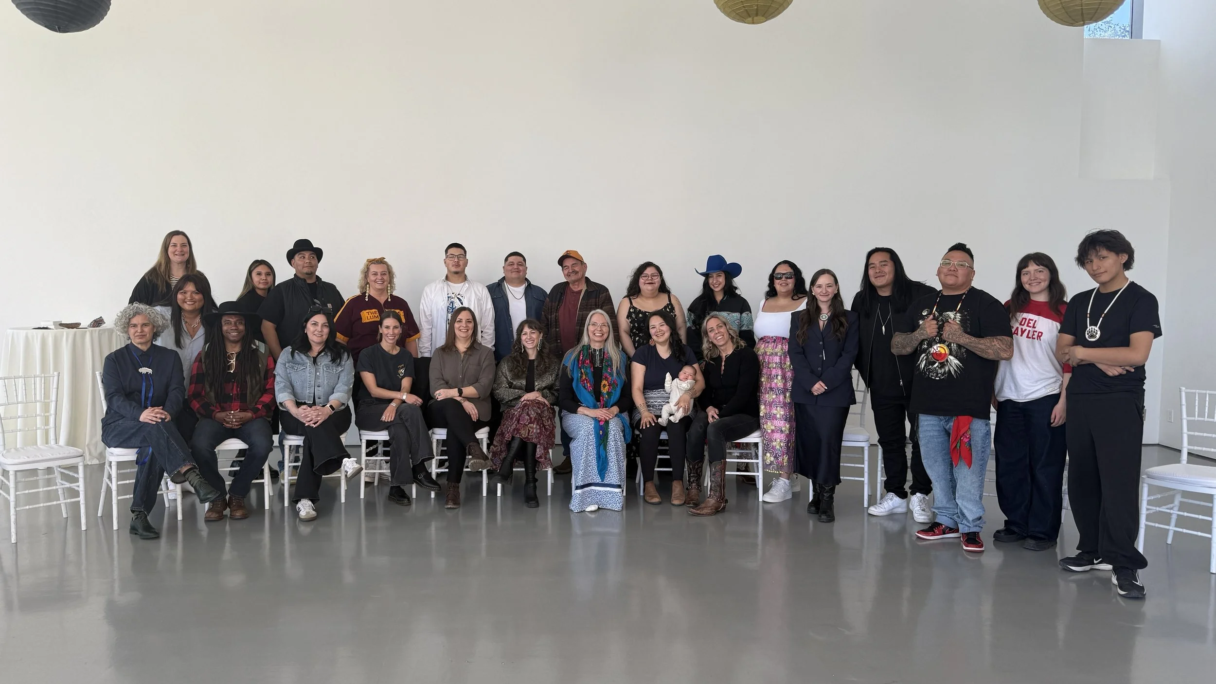 A wide-angle classroom-style photo with approximately 20 people seated and standing, smiling at the camera.