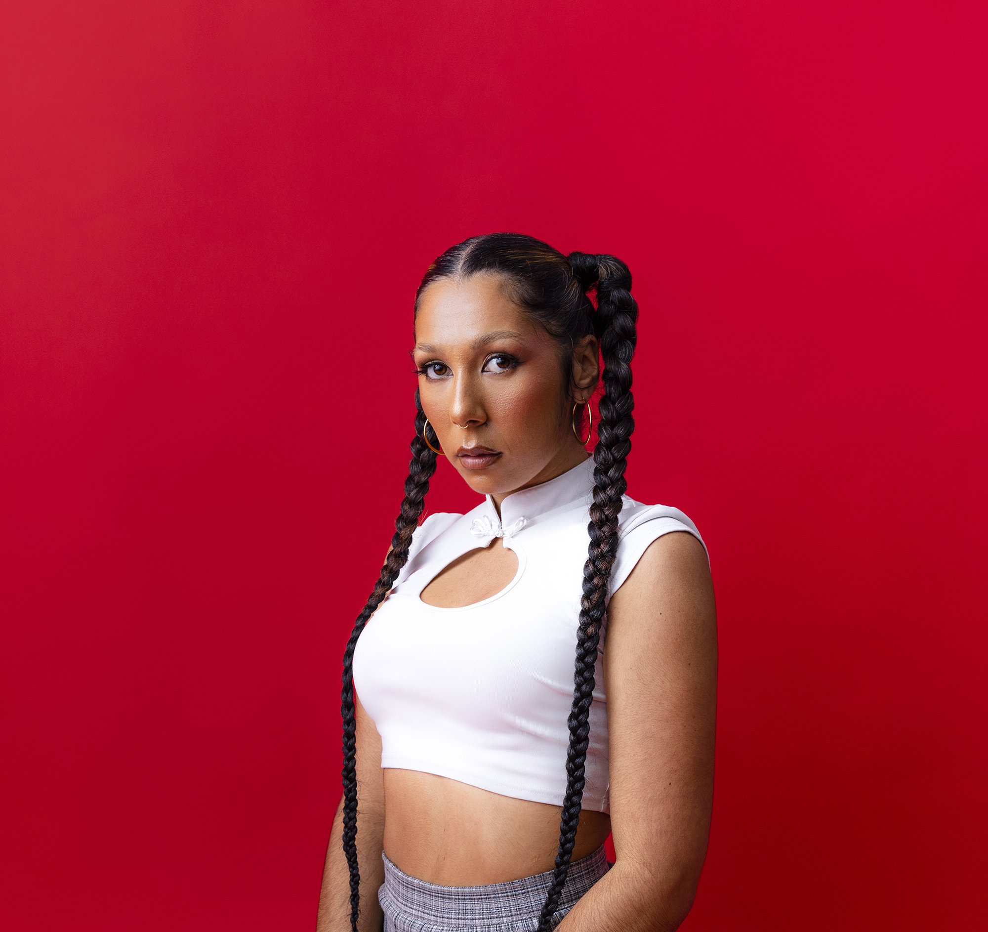 A press photo of female artist Miss Kaninna with long braids on a bright red backdrop.
