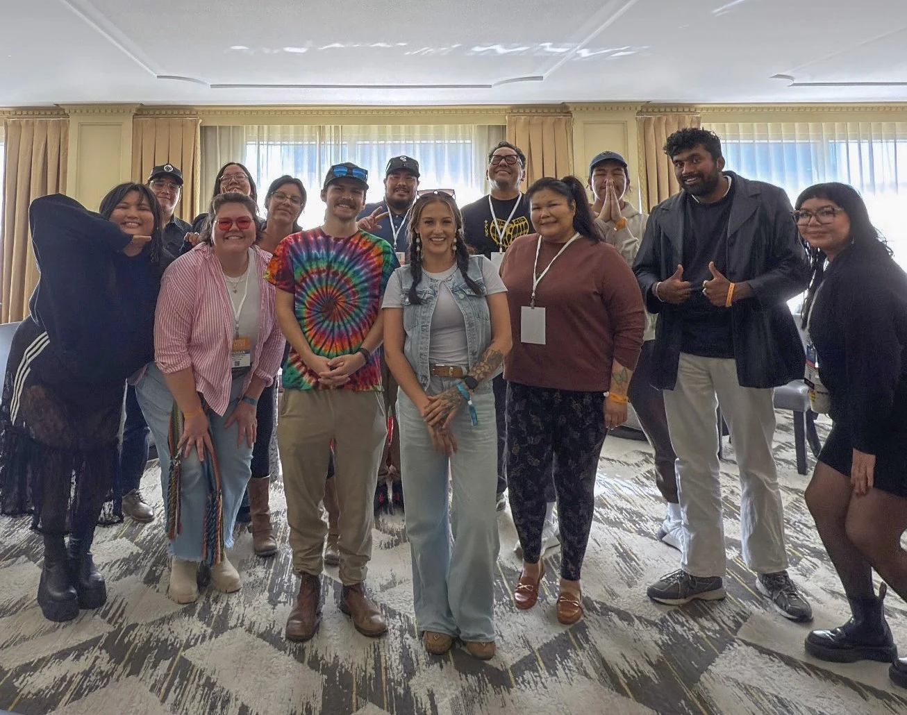 A photo of 10-15 people standing in a meeting room in a hotel, smiling at the camera.