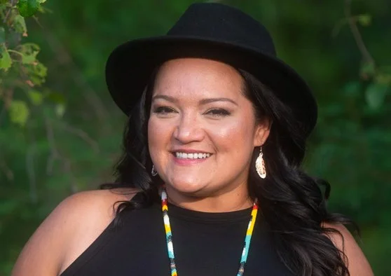 A photo of Candace Scott-Moore wearing a fedora and smiling at the camera.