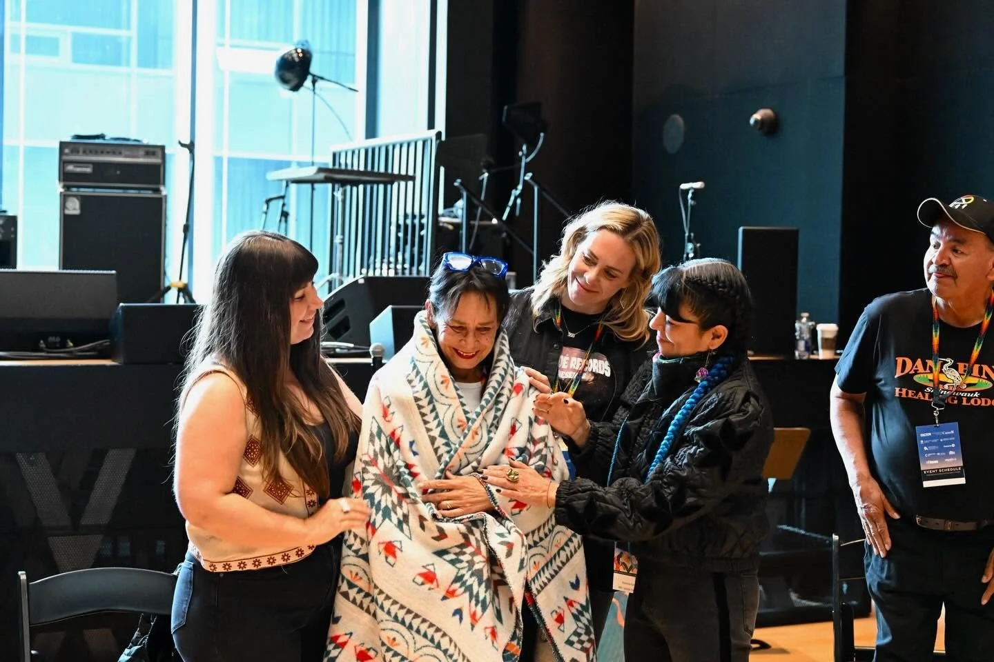 The late Rhoda Roberts is standing, wrapped in a traditional Indigenous blanket, surrounded by IIMS reps Nicole Auger, Amanda Rheaume and ShoShona Kish.