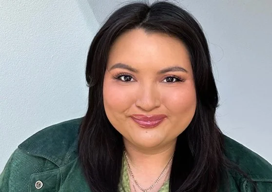 A photo of Nimkish Younging smiling at the camera, long, straight, dark hair, wearing a green jacket