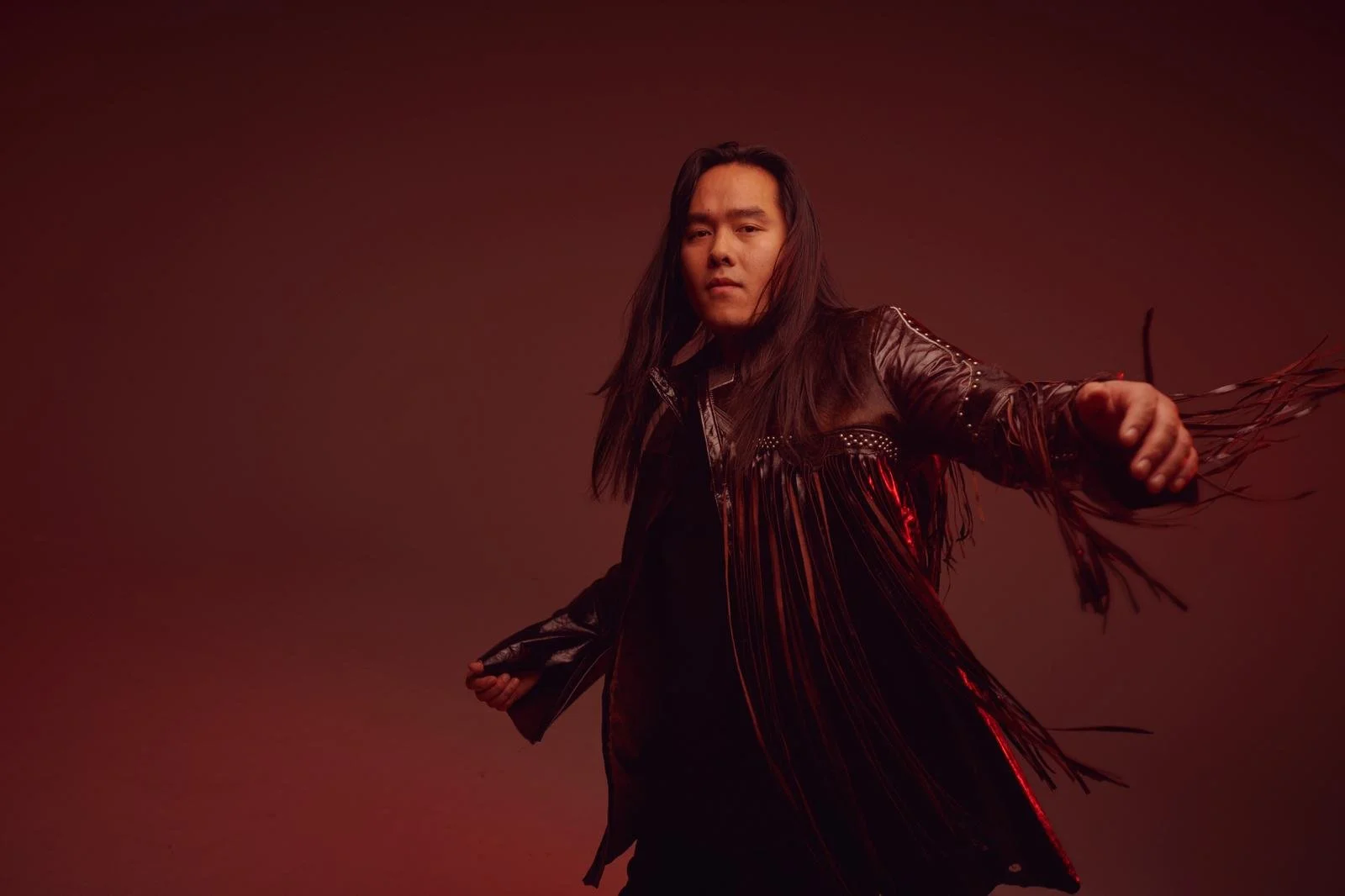 A press photo of male artist Aysanabee spinning in a fringe leather jacket.