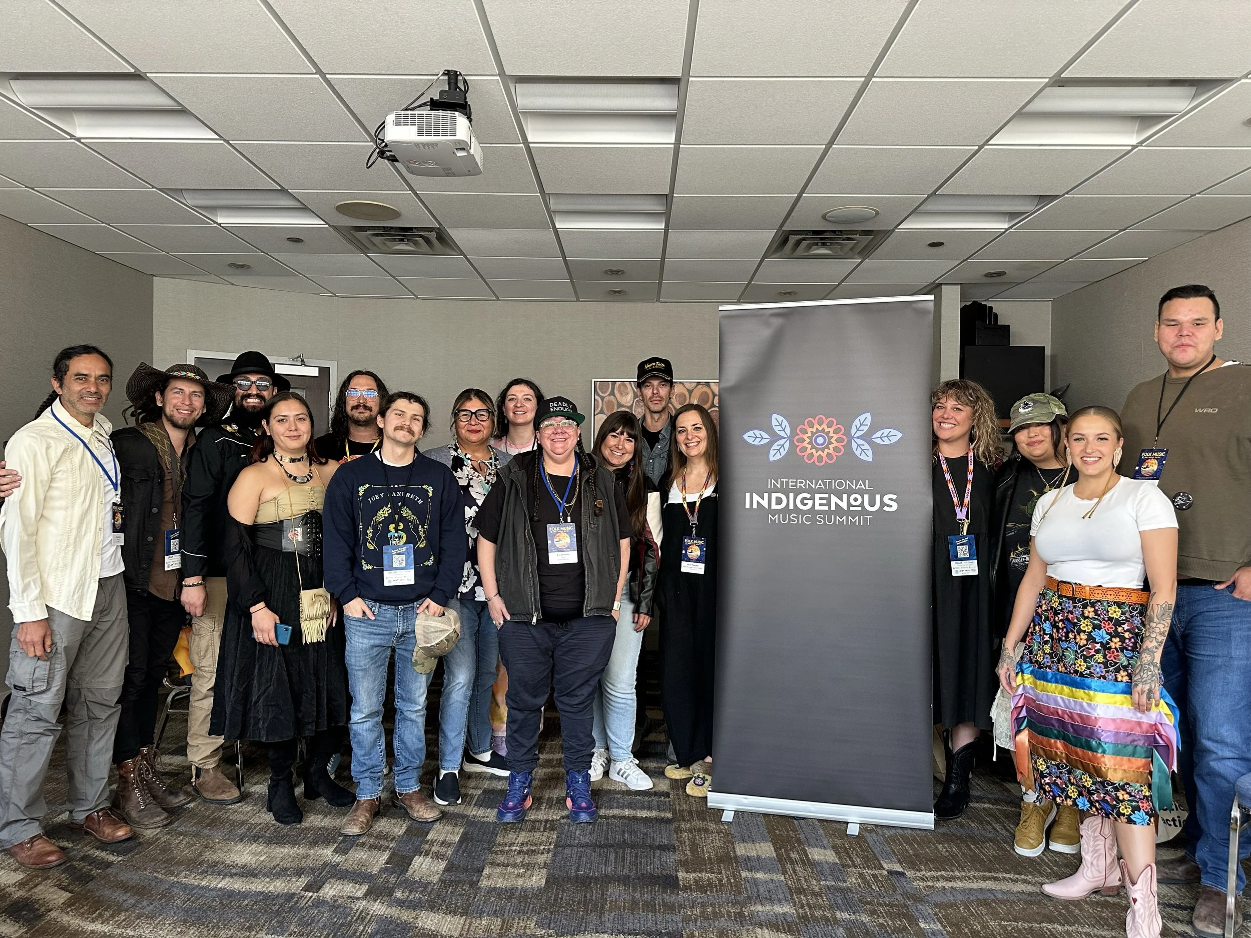 A photo of 10-15 people standing in a meeting room in a hotel, smiling at the camera.