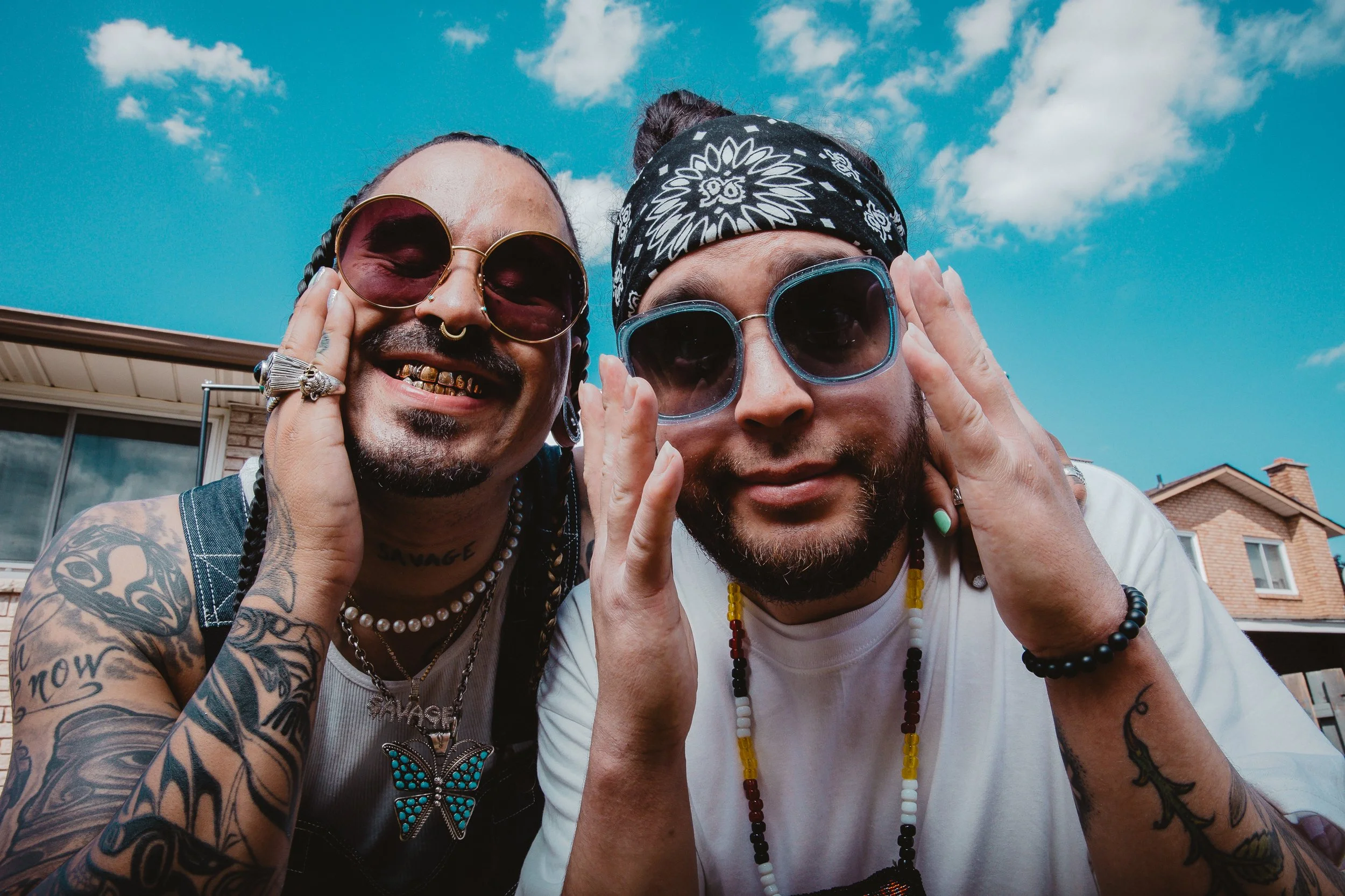 A close-up, fisheye-style press photo of Snotty Nose Rez Kids wearing sunglasses and smiling for the camera.