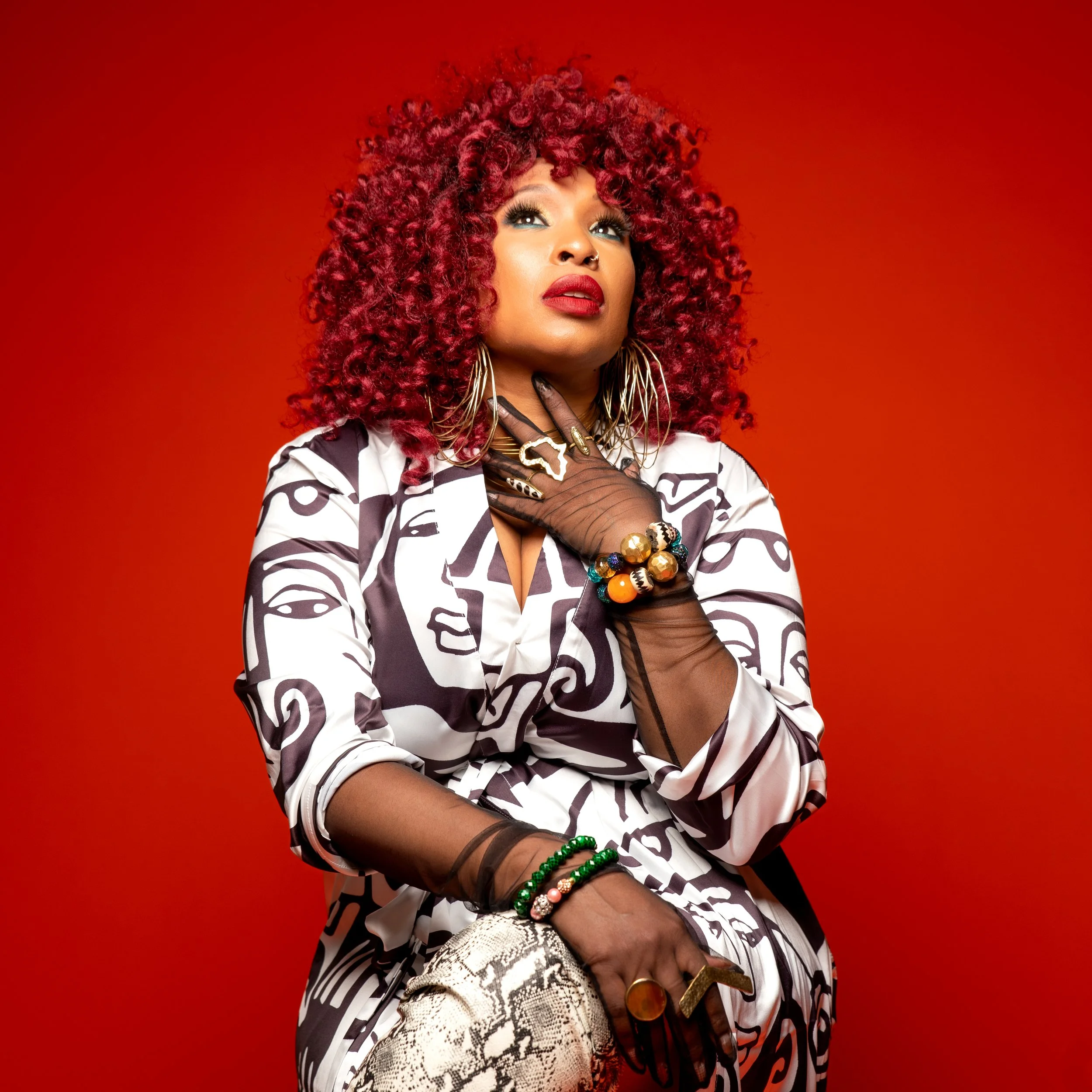 A press photo of female artist Mumu Fresh with bold patterned clothing on a dark red backdrop..