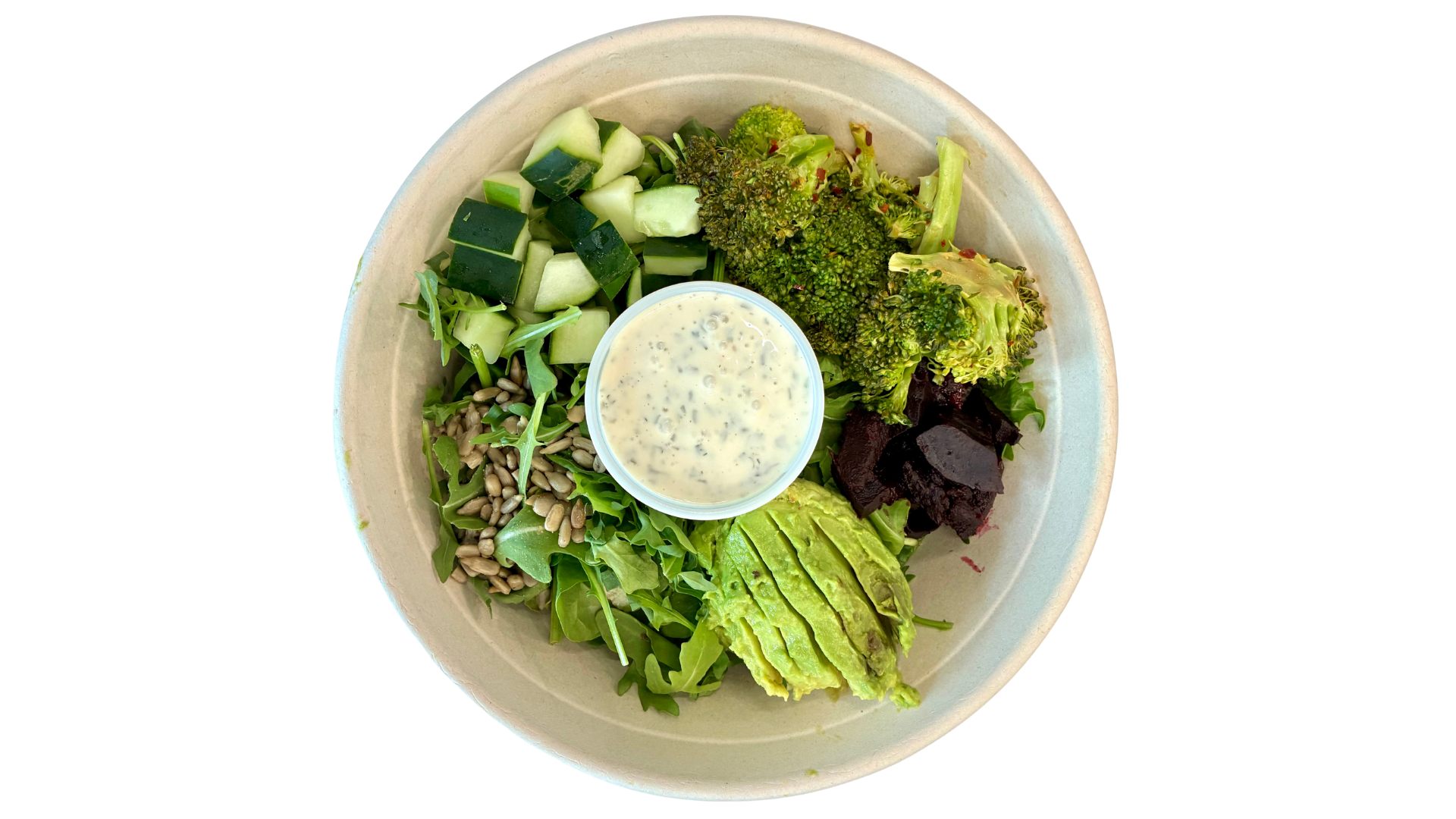 Mixed green salad with chopped cucumbers, broccoli, beets, sunflower seeds, and leafy greens, served with a side of ranch dressing in a small container, on a disposable bowl.