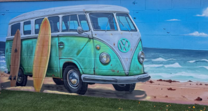 Mural of a vintage Volkswagen van with surfboards on the beach, depicting a wave and ocean in the background.