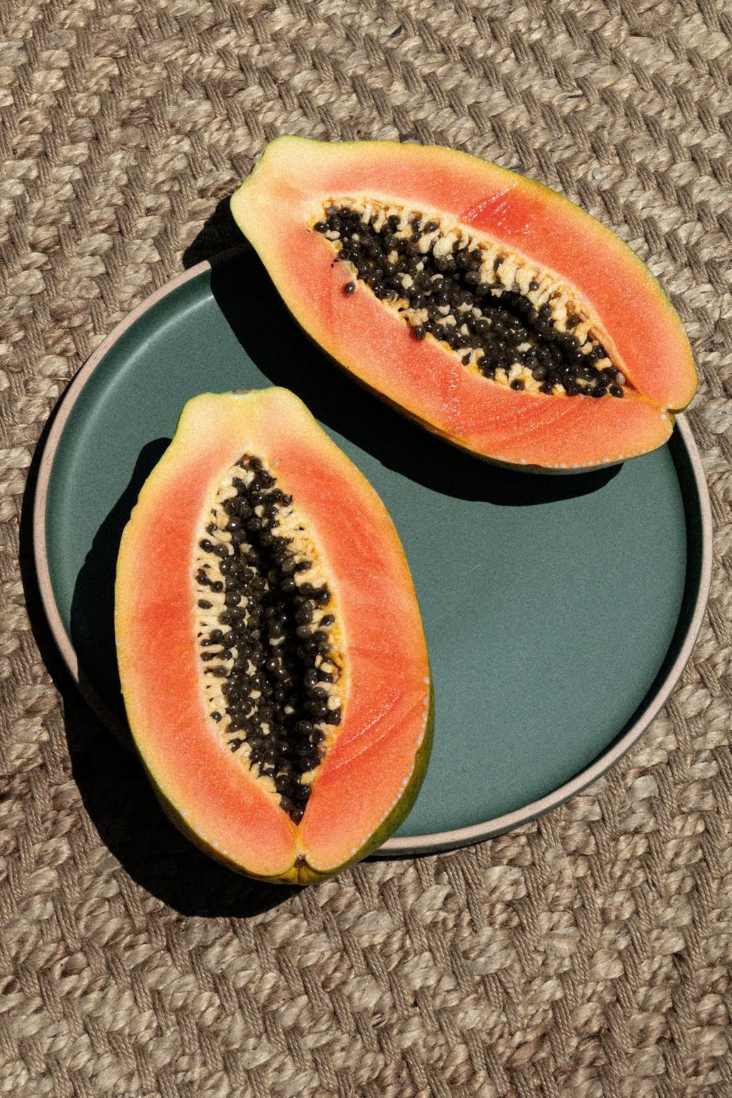 A sliced papaya fruit on a teal-colored plate, resting on a woven textured surface.