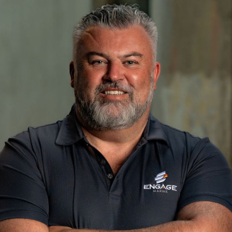 A smiling man with gray hair and beard wearing a black polo shirt with the 'ENGAGE MARINE' logo, standing in front of a neutral background.