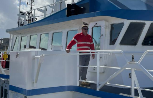 Man in red and white striped shirt standing on a boat's deck.